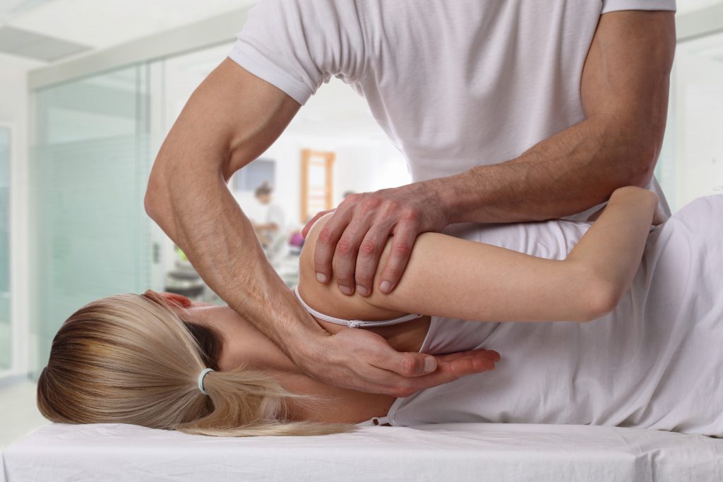 A physiotherapist mobilising a patient's shoulder and upper back on a treatment couch